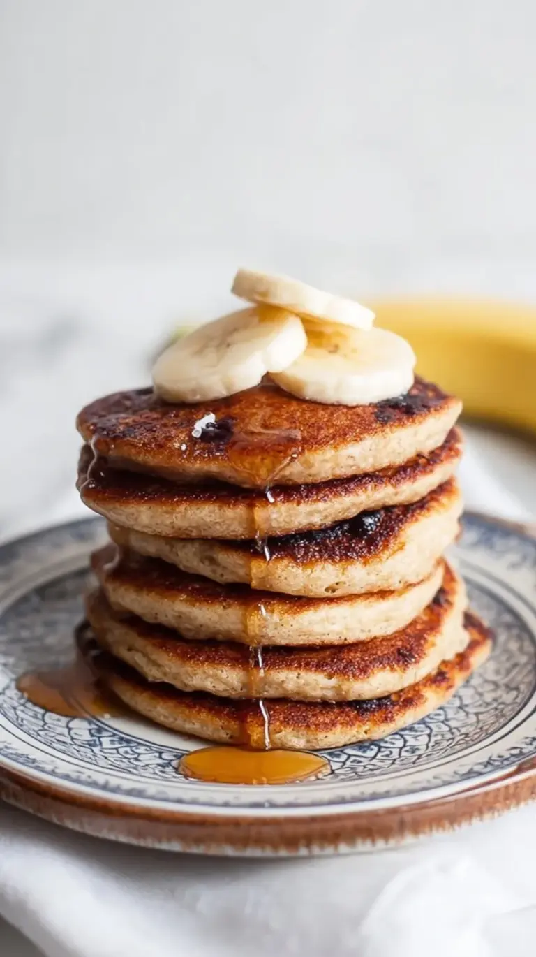 A stack of golden brown banana cottage cheese pancakes topped with fresh fruit and syrup