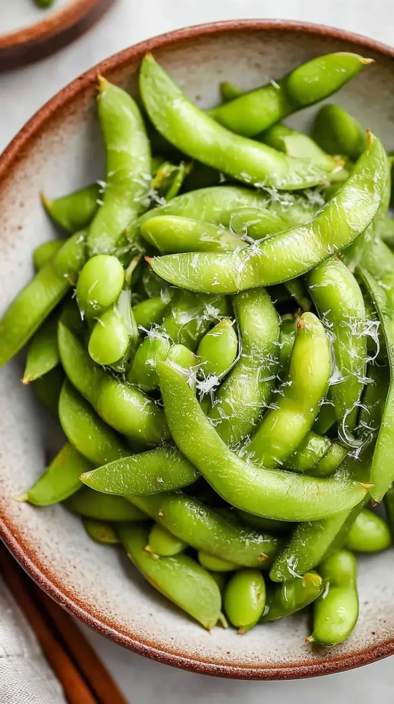A bowl of bright green steamed edamame pods sprinkled with flaky sea salt