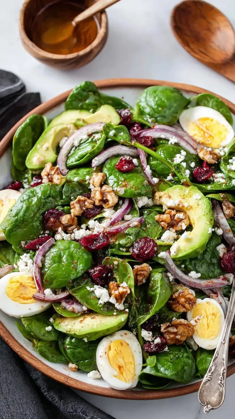 A fresh spinach salad with sliced eggs, red onions, and pecans in a glass bowl