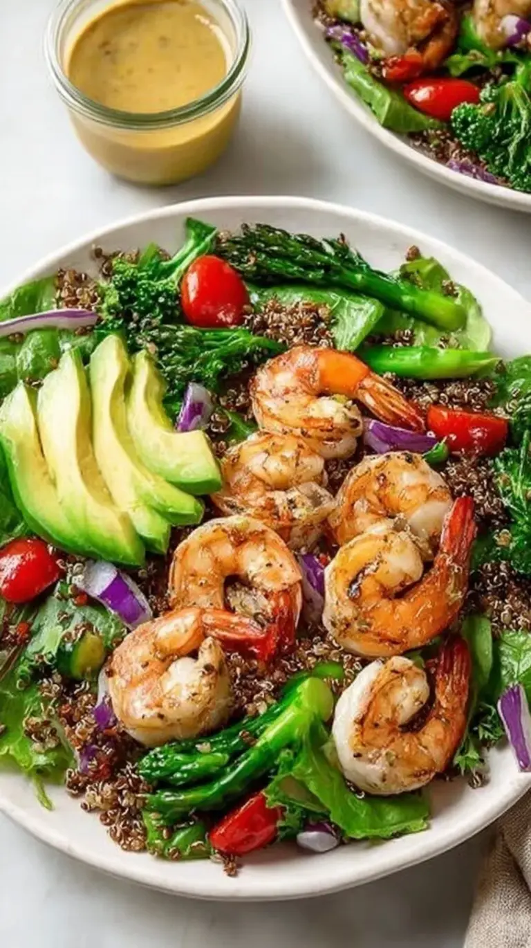 A vibrant grilled shrimp salad with cherry tomatoes, cucumbers, and feta cheese on a white plate.
