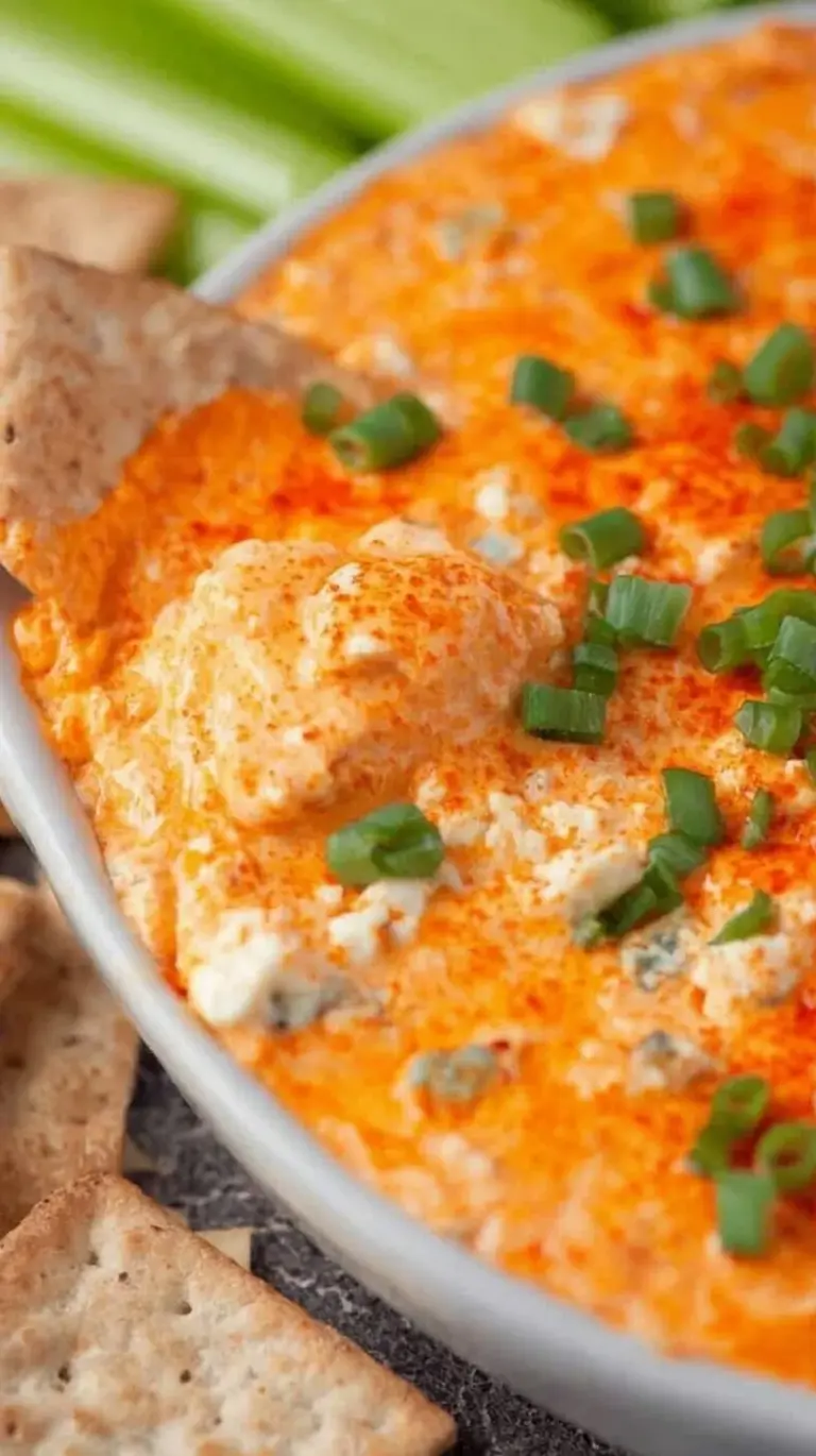 A warm dish of bubbly buffalo chicken dip topped with green onions and melted cheese.