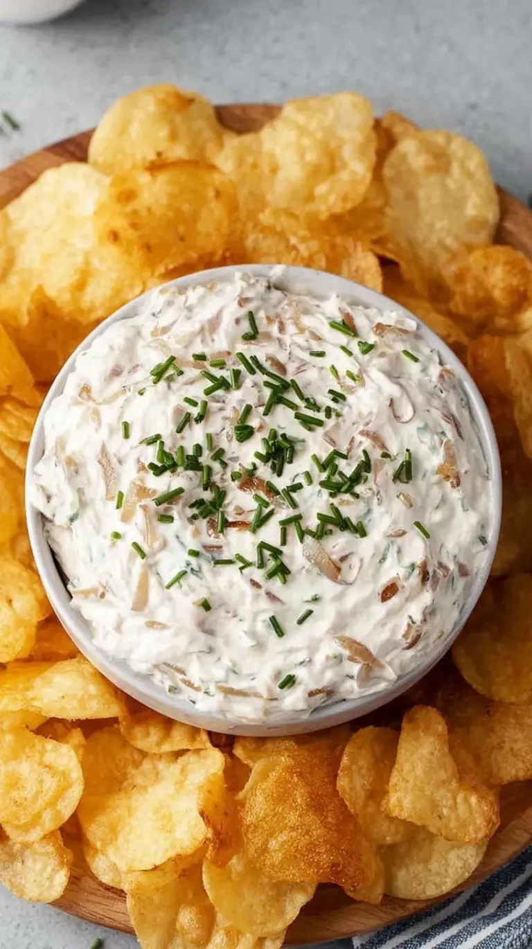 A bowl of creamy Greek yogurt onion dip topped with fresh chives and served with vegetable sticks.