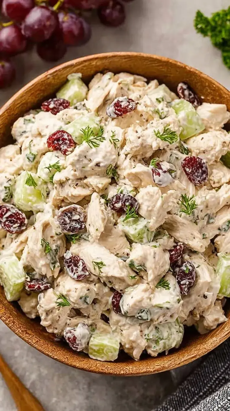 A bright bowl of creamy chicken salad with fresh dill and celery on a light wooden table.
