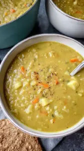 A steaming bowl of thick green split pea soup with shredded turkey on top