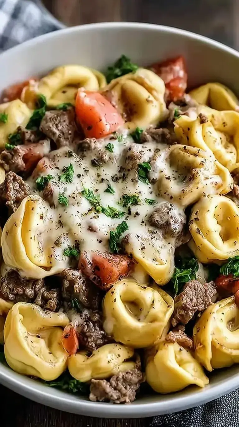 A skillet filled with creamy Philly cheesesteak tortellini pasta, featuring sliced steak, green peppers, and melted provolone cheese.