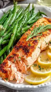 A sheet pan with roasted salmon fillets topped with lemon slices and tender green beans.