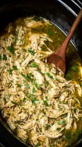 Shredded chicken in green salsa inside a slow cooker, garnished with fresh cilantro and lime